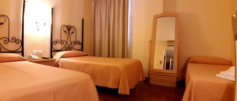 Habitación de hotel con dos camas, una mesita de noche con teléfono, un espejo y una ventana con cortinas.