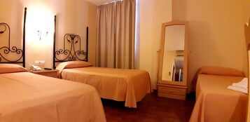 Habitación de hotel con dos camas, una mesita de noche con teléfono, un espejo y una ventana con cortinas.