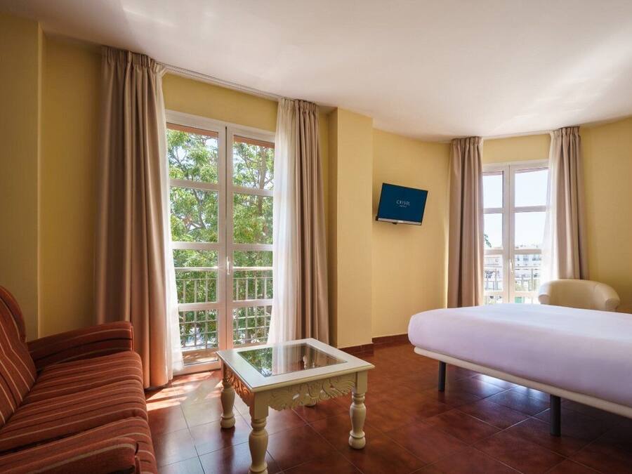 A hotel room with a bed, a sofa, a small table, and a TV on the wall.