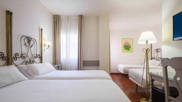 Hotelkamer met twee bedden, een bureau, een stoel, een lamp, een schilderij en een raam met gordijnen.