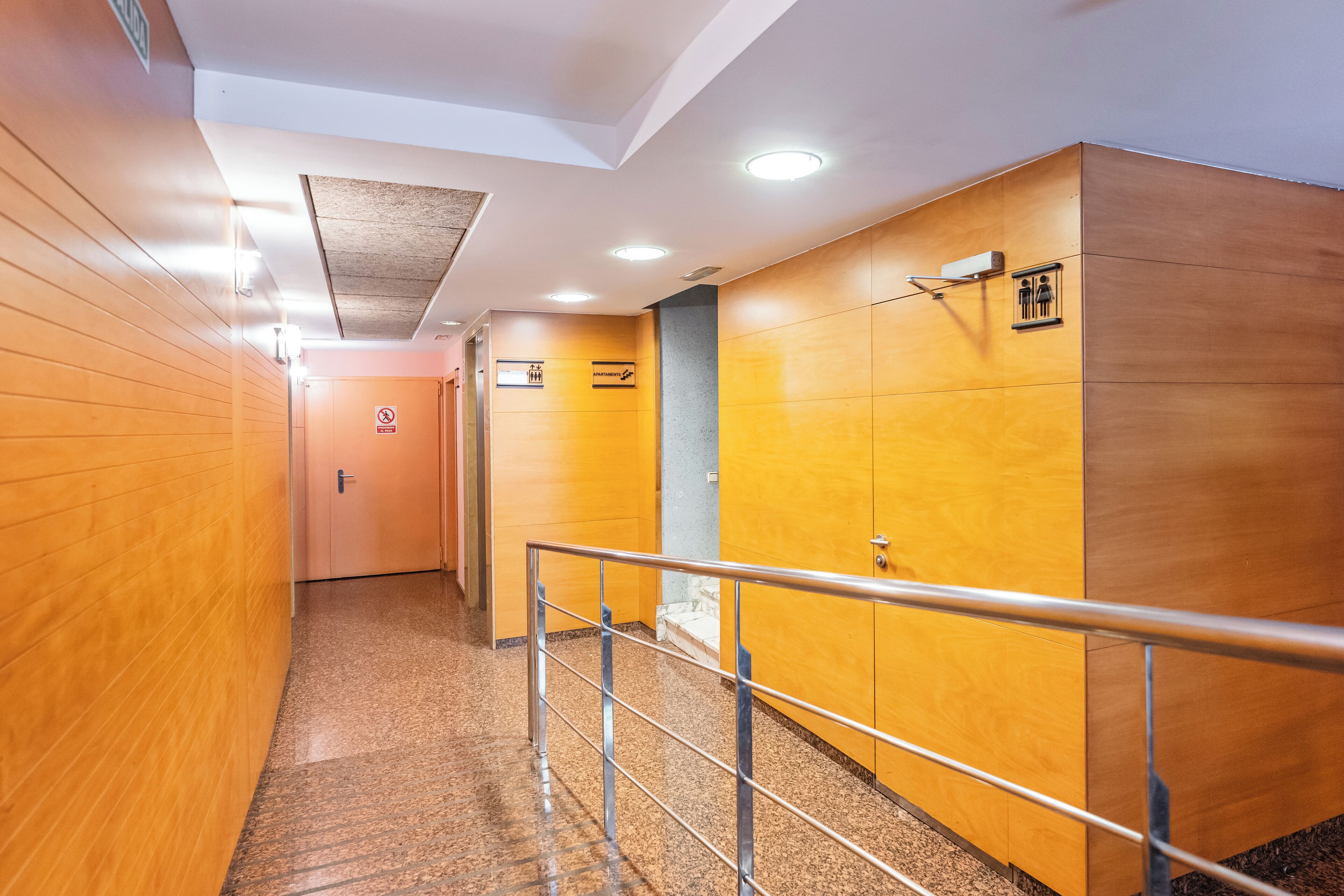 A hallway with wooden walls, a metal railing, and a door at the end.
