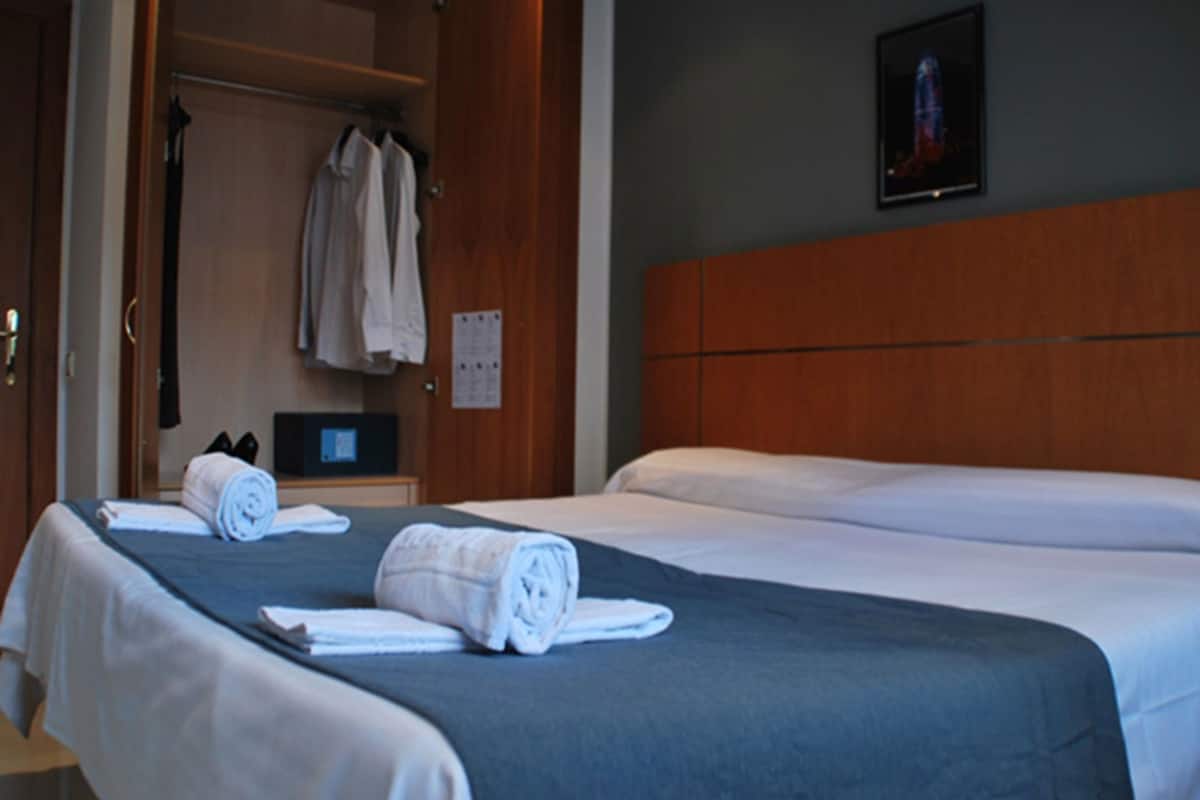 Une chambre d’hôtel avec deux lits, une tête de lit en bois, une armoire et un petit bureau avec un ordinateur.