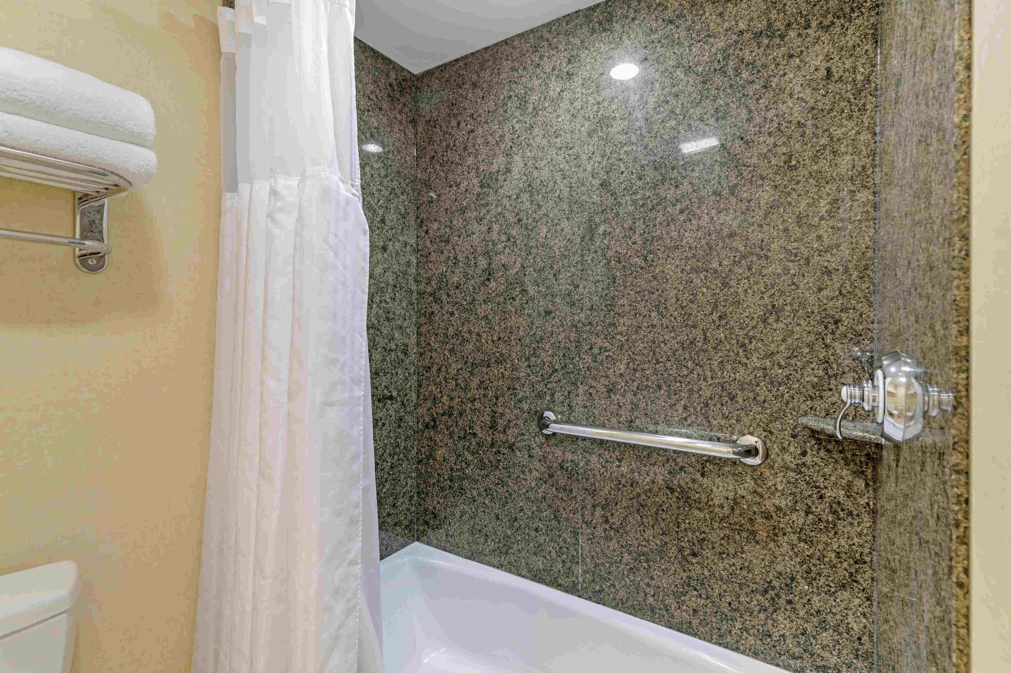 A bathroom with a granite wall, a white bathtub, and a towel rack.