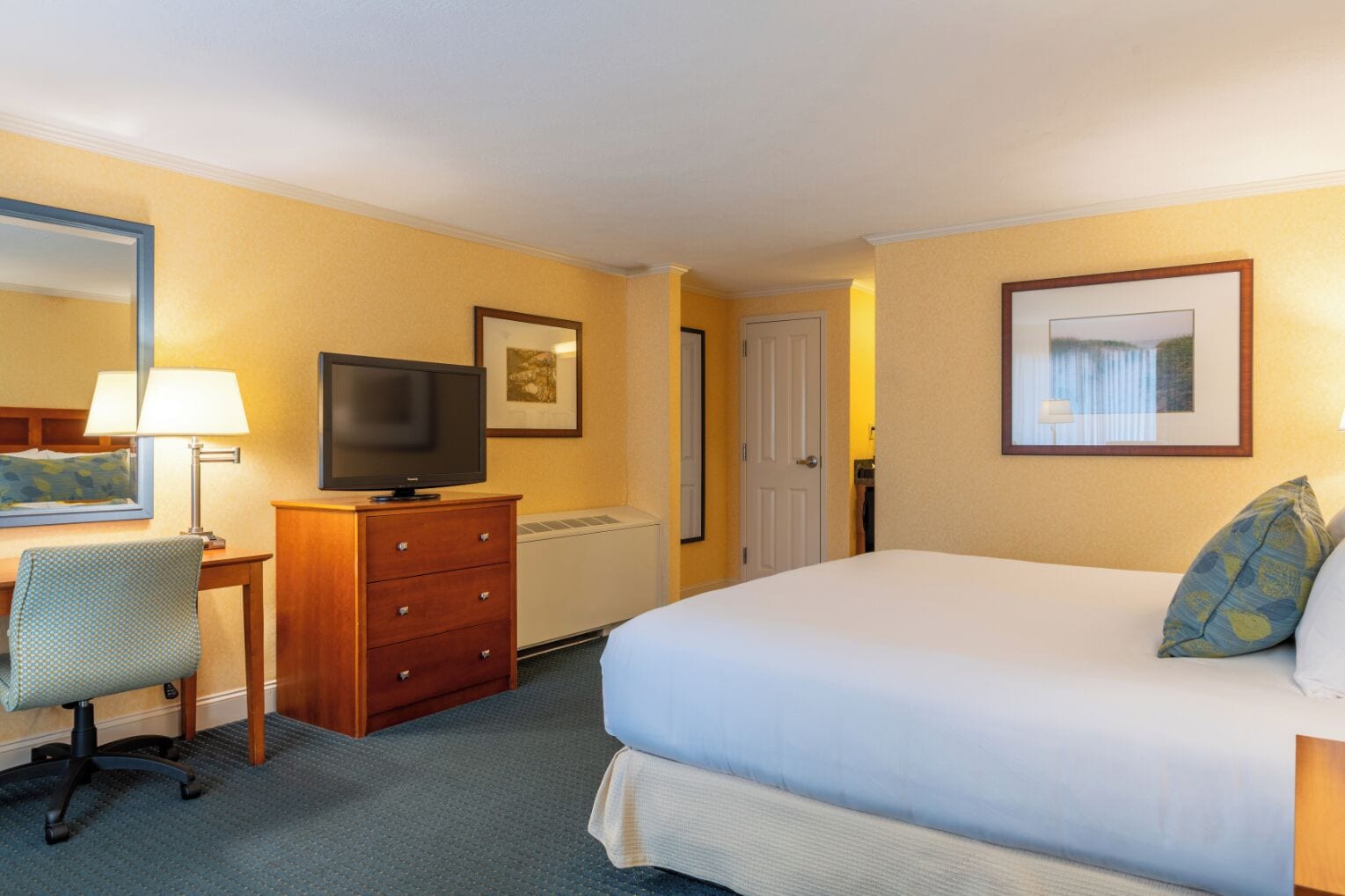Une chambre d’hôtel comprenant un lit, un bureau avec une chaise, une télévision, une commode et une porte.
