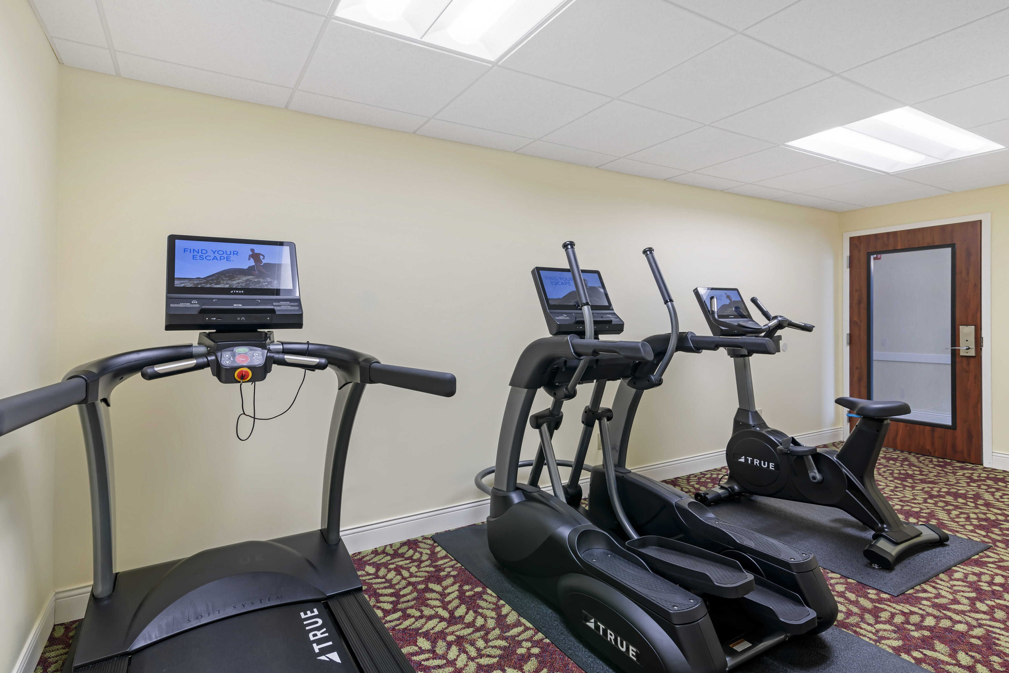 A fitness room with three treadmills, a stationary bike, and a rowing machine.