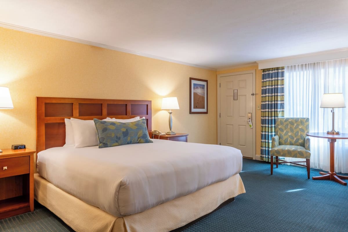 A hotel room with a large bed, a chair, a nightstand, and a lamp.