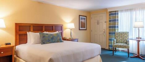 A hotel room with a large bed, a chair, a nightstand, and a lamp.