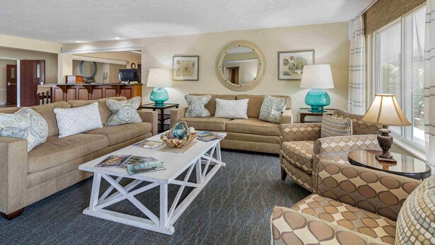 A living room with a sofa, armchair, coffee table, and lamps. There is a kitchen area in the background. - Juniper Hill Inn (Ogunquit)