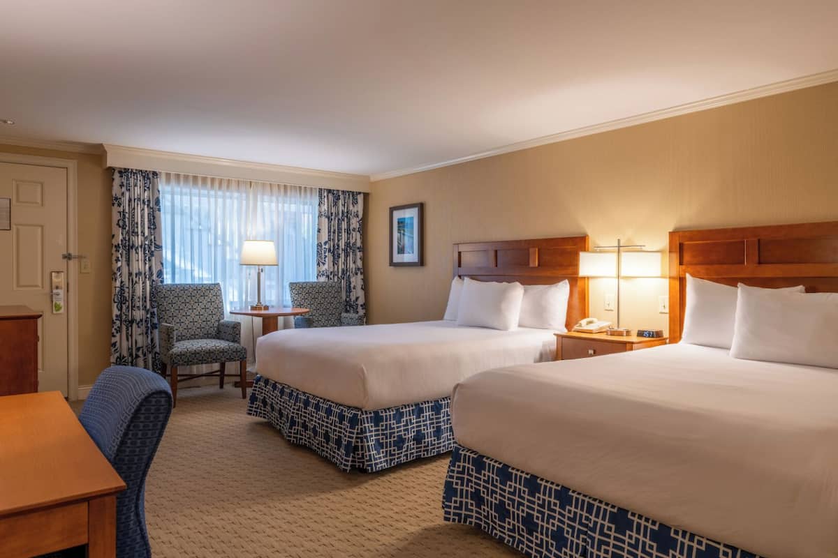 A hotel room with two beds, a desk, a chair, and a window with curtains.