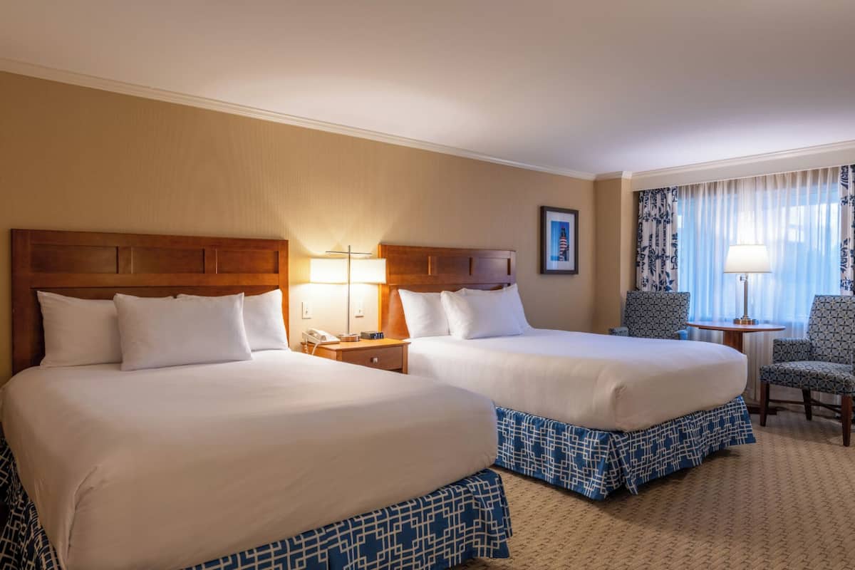A hotel room with two beds, a desk, a chair, and a window with curtains.