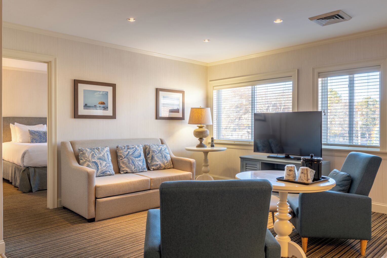 A hotel room with a bed, a sofa, a TV, and a small table with a lamp.