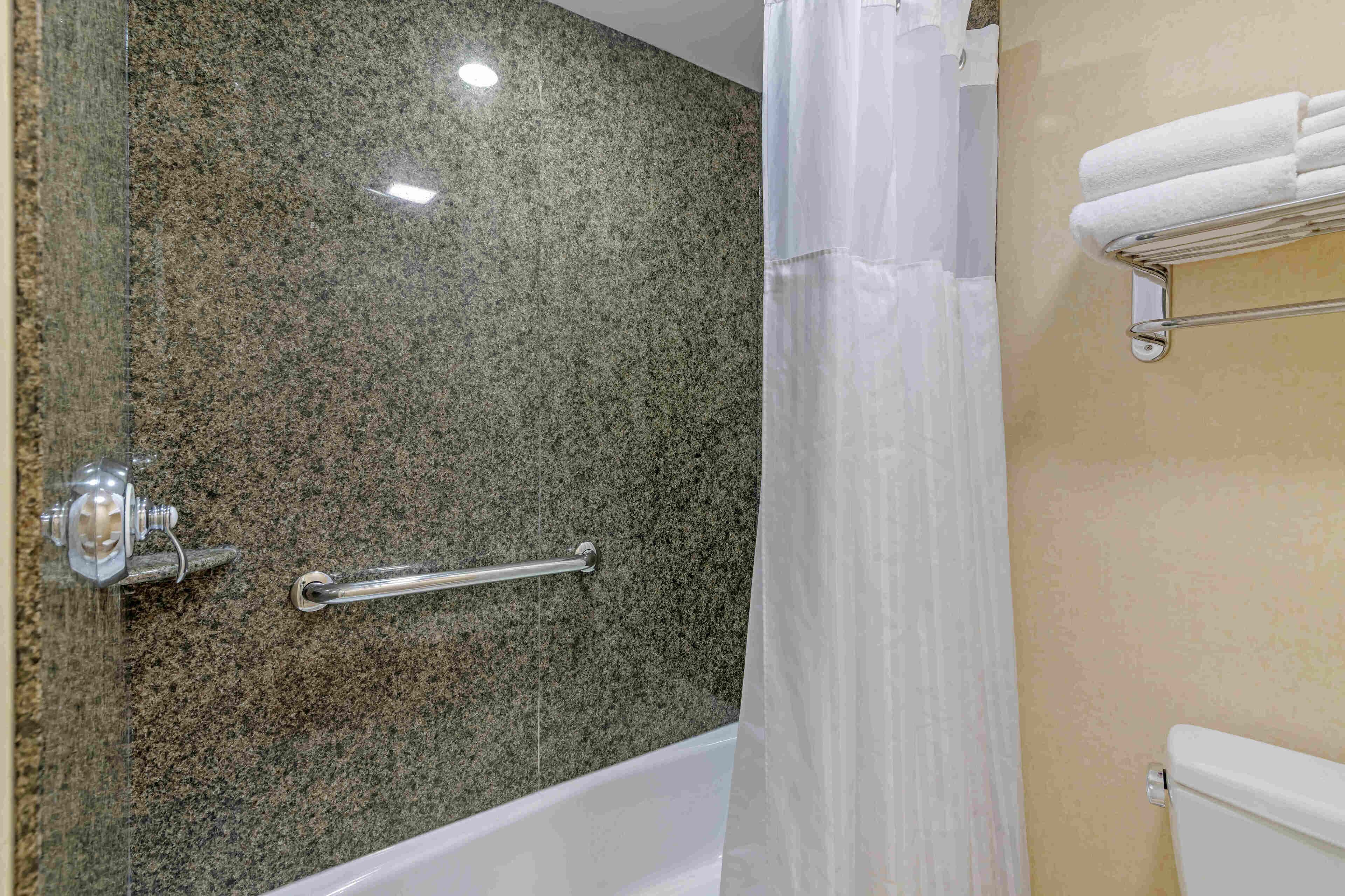 A bathroom with a granite wall, a shower curtain, a grab bar, and a towel rack.
