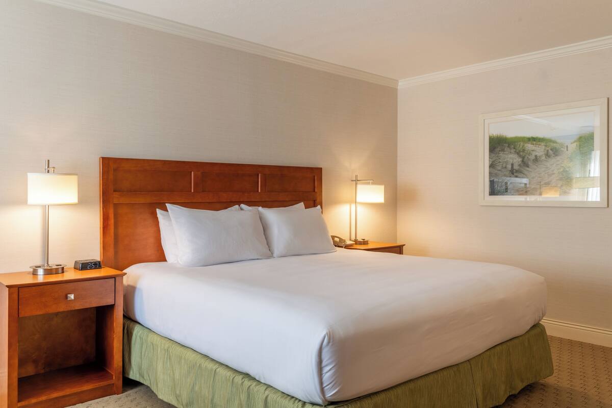 A neatly made bed with white linens, two bedside lamps, a wooden nightstand, and a framed picture on the wall.