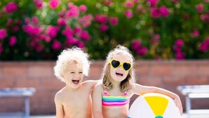 Two children sitting by a pool with a beach ball, surrounded by a brick wall and pink flowers. - Juniper Hill Inn (Ogunquit)