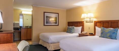 A hotel room with two beds, a desk, a chair, a nightstand, a lamp, and a framed picture on the wall.