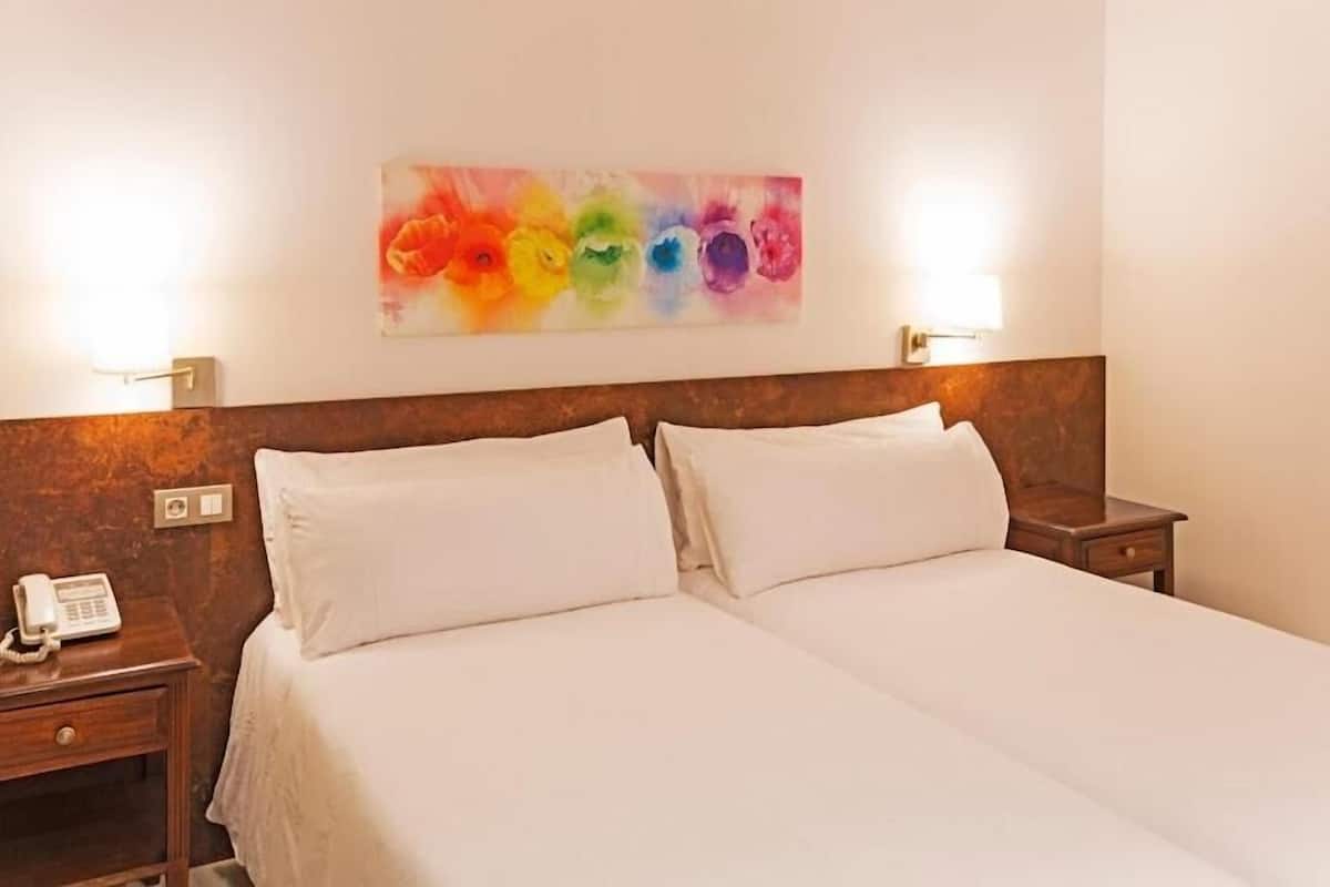Une chambre d’hôtel avec deux lits, un tableau au mur et des lampes de chevet.