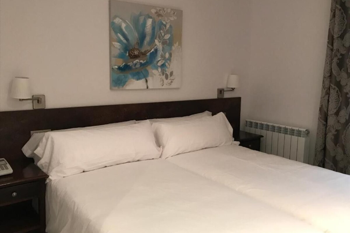 Una habitación de hotel con una cama grande, dos mesitas de noche, una lámpara de pared y un radiador.