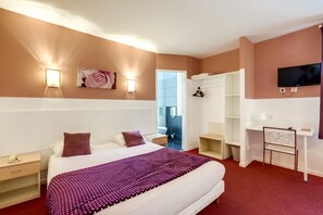 A hotel room with a large bed, a desk, a chair, a TV, and a wardrobe. - Citotel Du Midi (Narbonne)