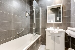 A modern bathroom with a bathtub, shower, and vanity. - Citotel Du Midi (Narbonne)