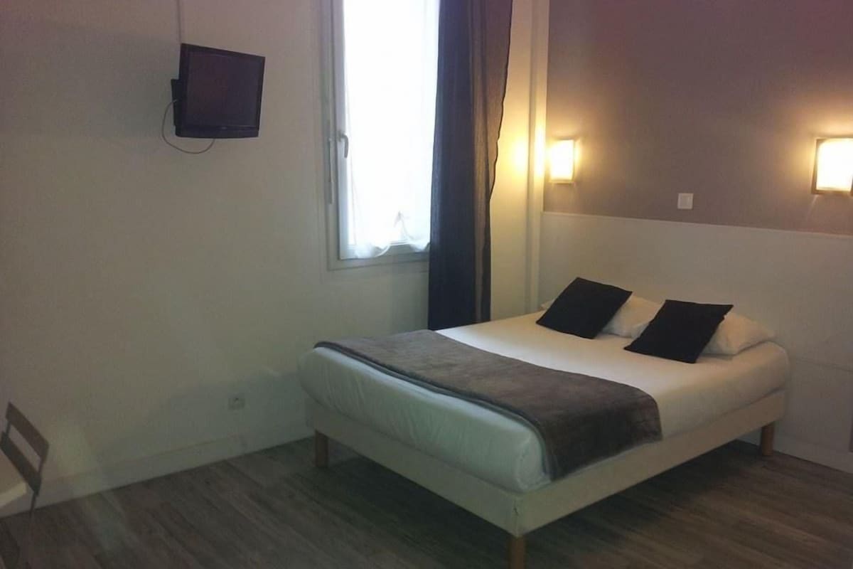 A bedroom with a bed, a TV mounted on the wall, and two wall-mounted lights.