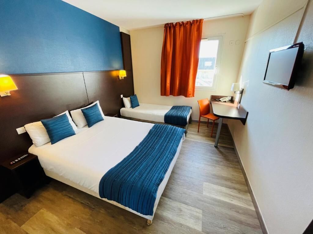 A hotel room with two beds, a desk, a chair, a TV, and a window with curtains.