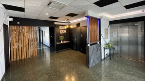 Een moderne lobby met een receptiebalie, een houten scheidingswand en een lift.