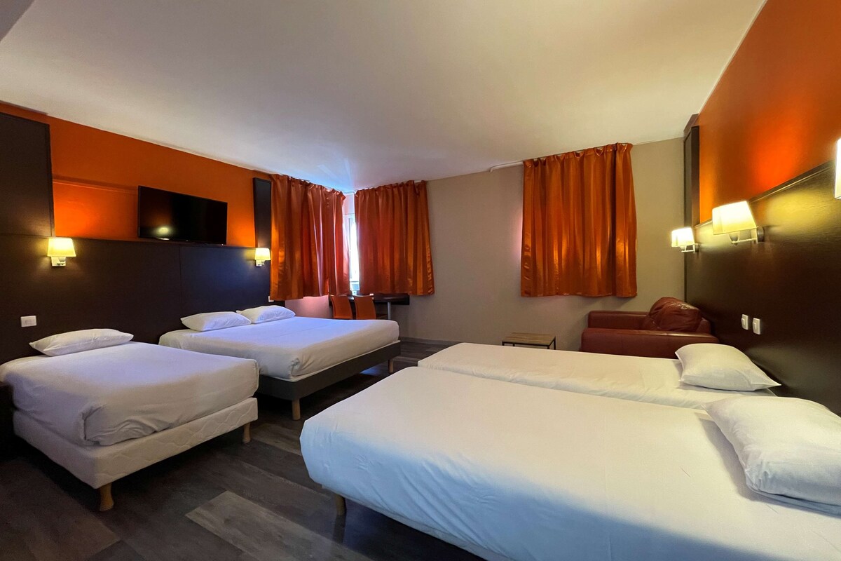 A hotel room with two single beds, a double bed, a small table, and a sofa.