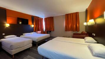 A hotel room with two single beds, a double bed, a small table, and a sofa.