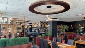 Een restaurantinterieur met houten tafels, zwarte stoelen en een bar in het midden.