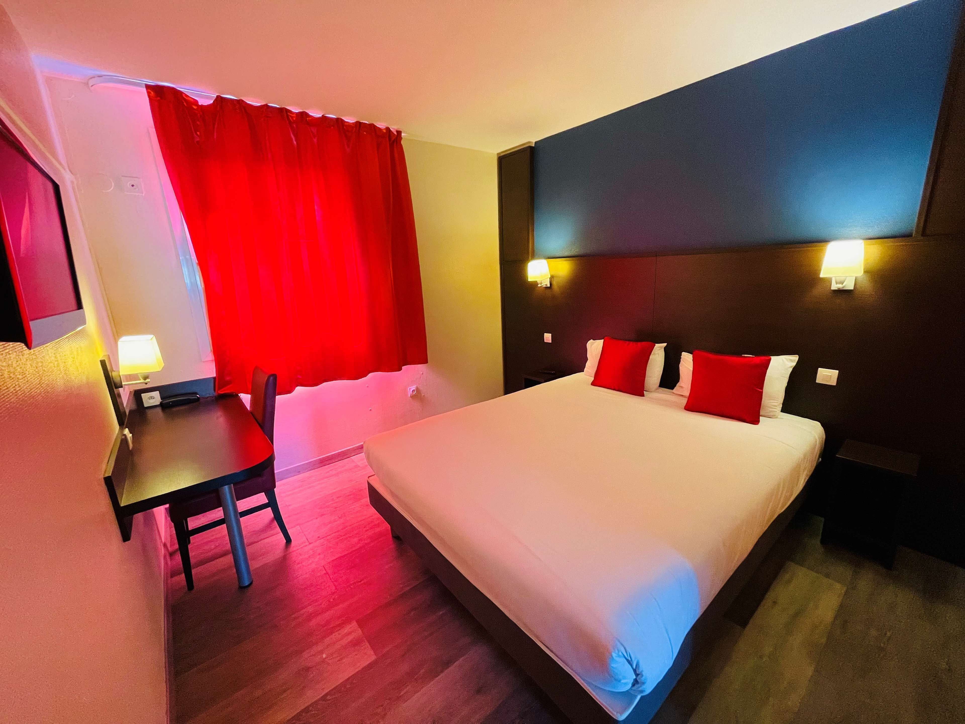Une chambre d’hôtel avec un grand lit, un bureau et une chaise. Il y a deux tables de chevet et une lampe fixée au mur.