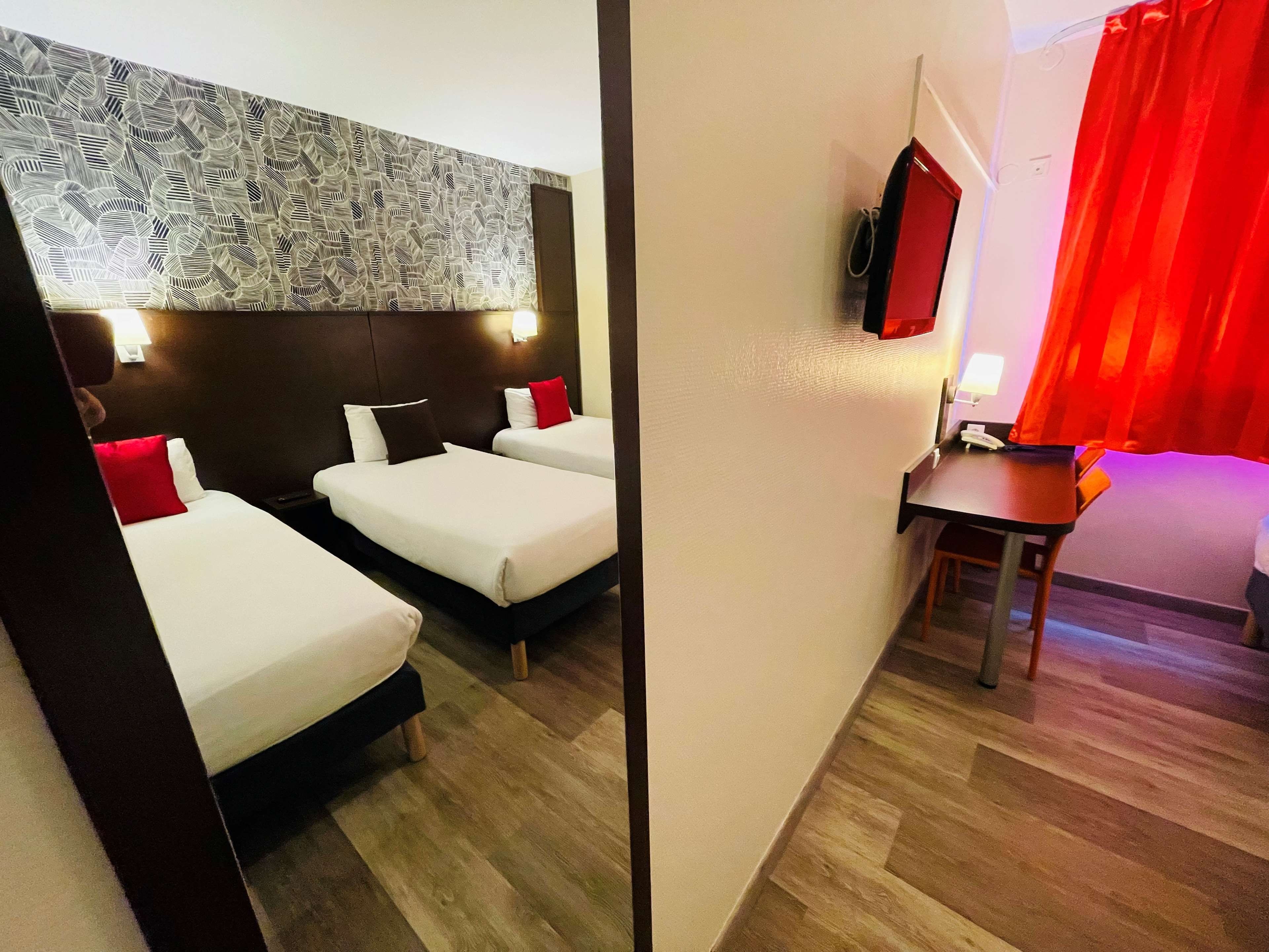 A hotel room with two beds, a desk, a chair, a TV, and a red curtain.