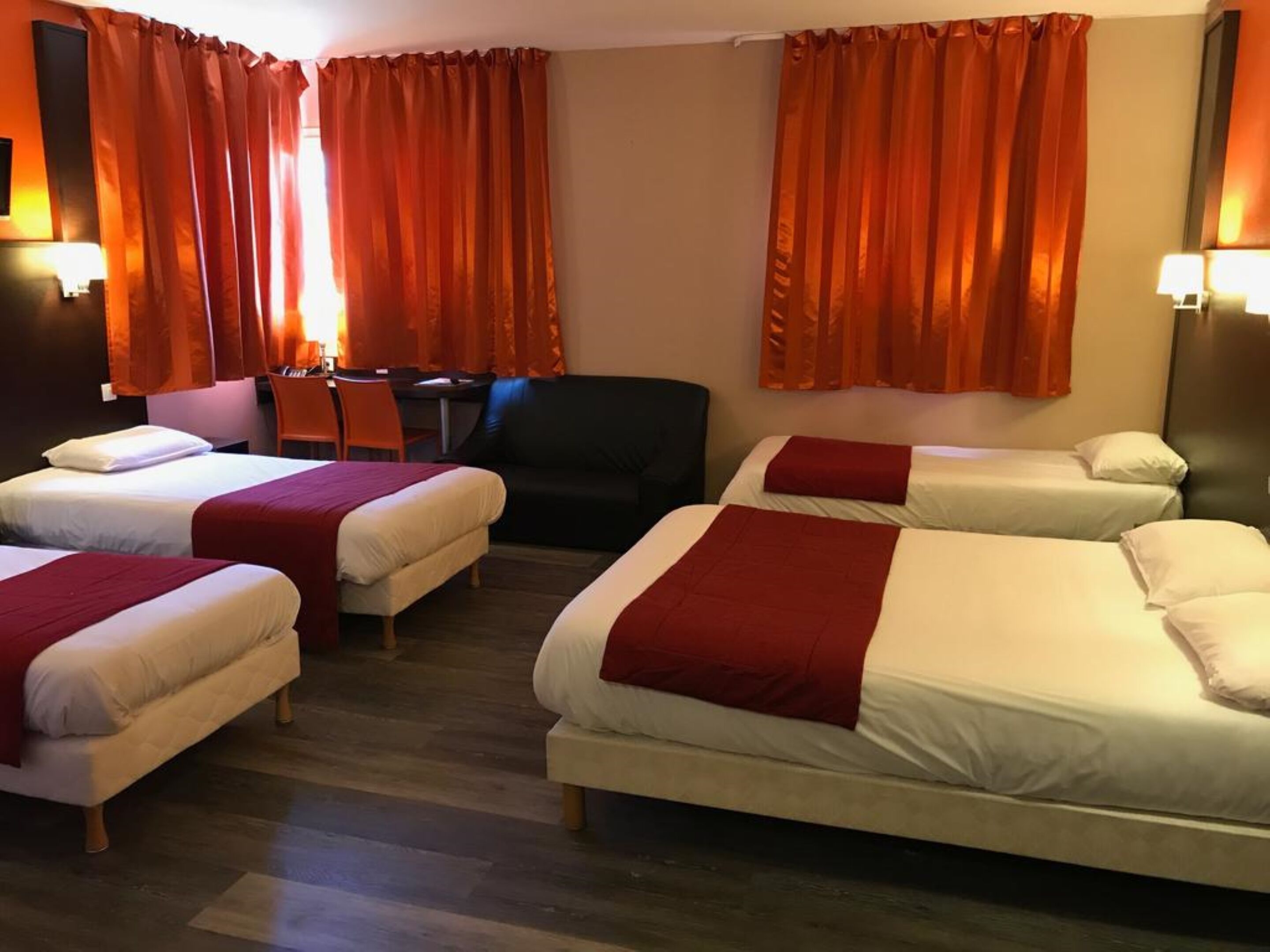 Habitación de hotel con cuatro camas, un escritorio y dos sillas.