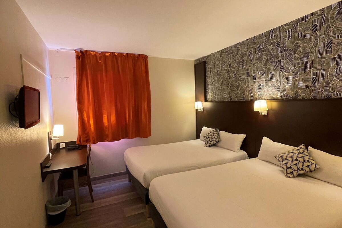 A hotel room with two beds, a desk, a chair, a trash bin, and a patterned wall.