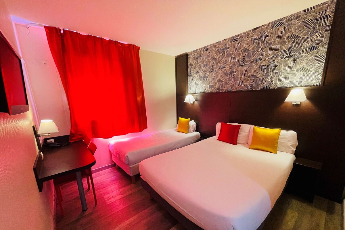 A hotel room with two beds, a desk, and a red curtain.