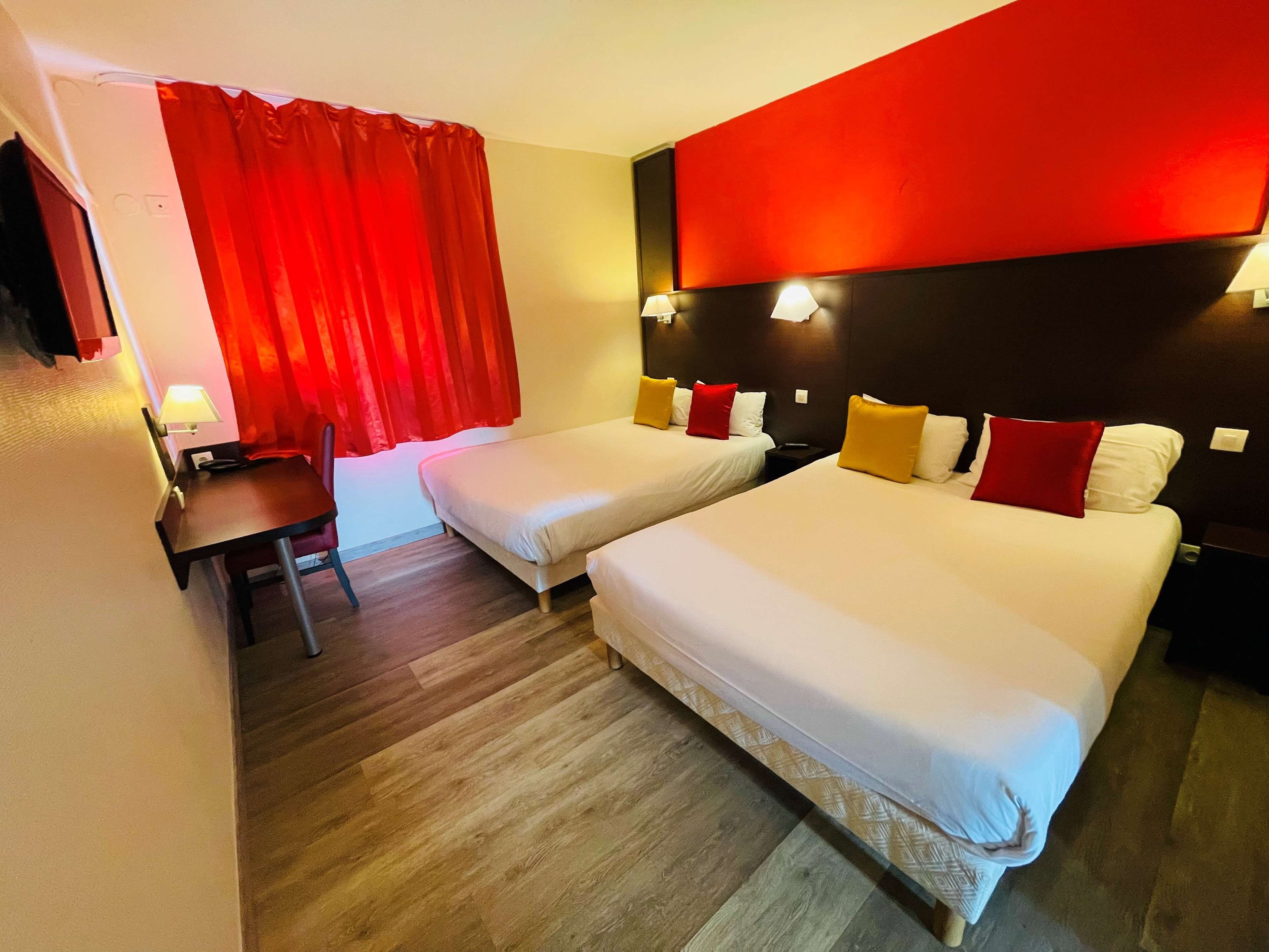 A hotel room with two beds, a desk, and a chair.
