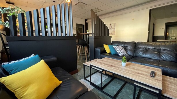 Een moderne zithoek met een zwarte leren bank, een houten salontafel en een frame van zwart metaal.