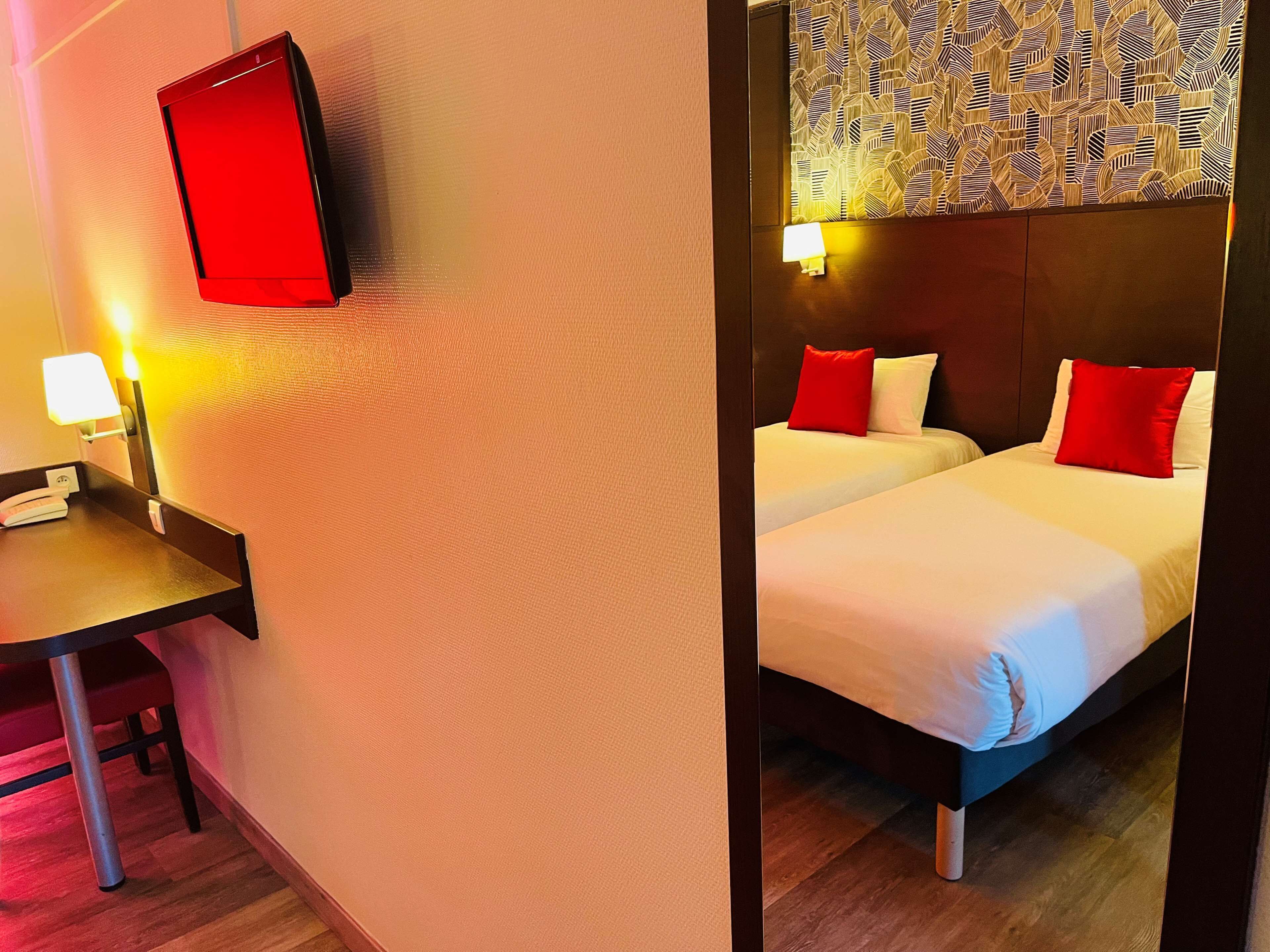 Une chambre d’hôtel équipée d’un bureau, d’un lit avec deux oreillers et d’un téléviseur fixé au mur.