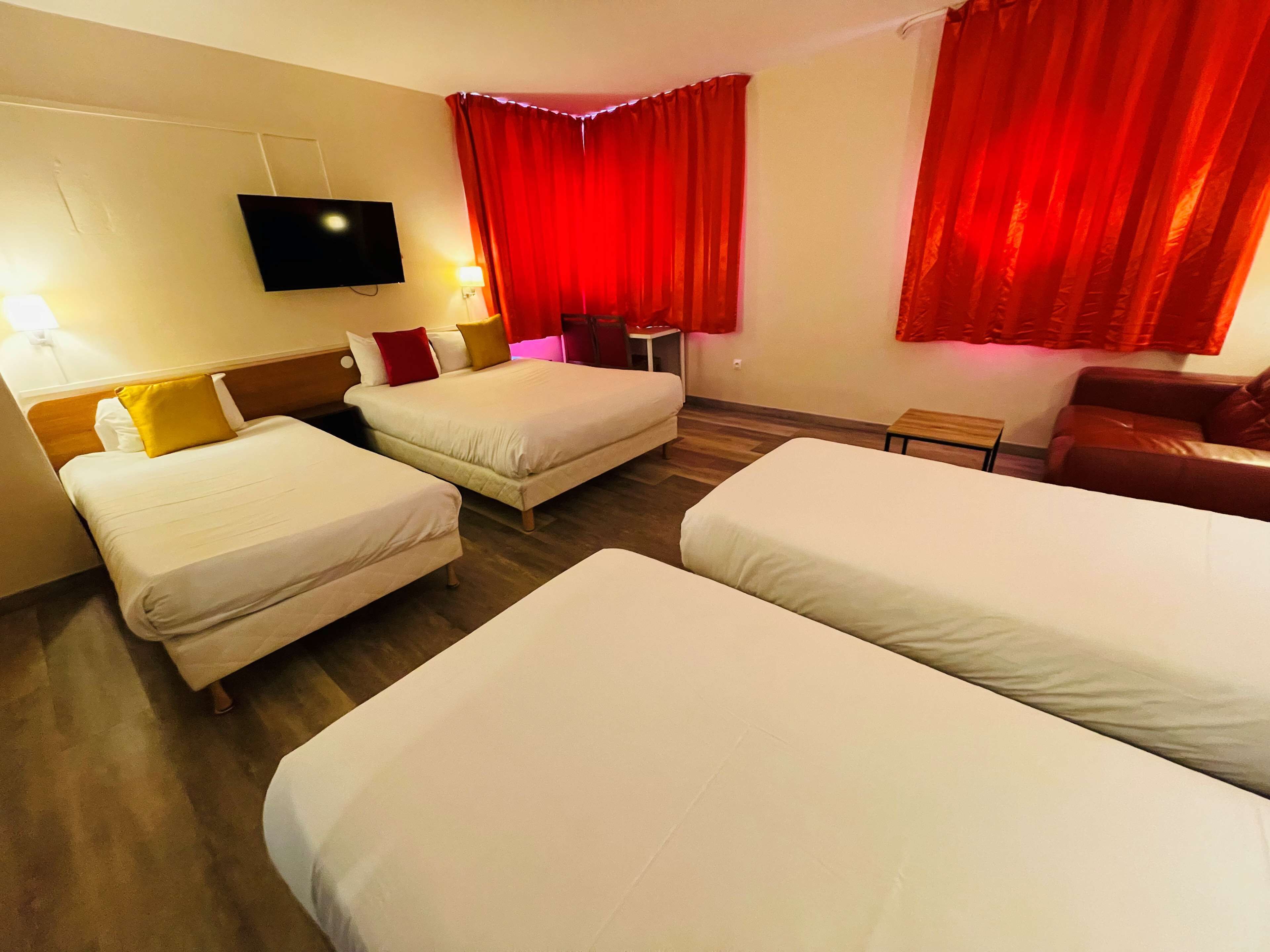 Une chambre d’hôtel avec deux lits simples, un téléviseur fixé au mur et des rideaux rouges.