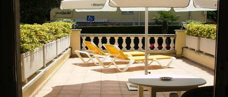 Un patio al aire libre con sillones amarillos y una mesa bajo un paraguas blanco.