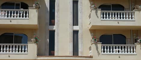 A multi-story building with a central entrance, balconies, and a tiled walkway leading to the entrance.