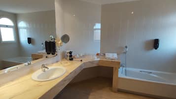 A modern bathroom with a large mirror, two sinks, a bathtub, and a window.