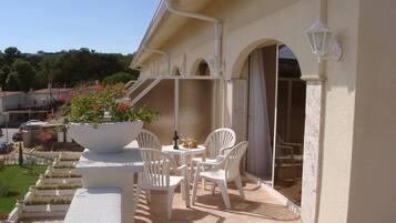 Un patio al aire libre con sillas y una mesa blancas, una maceta grande con flores y vistas del entorno.