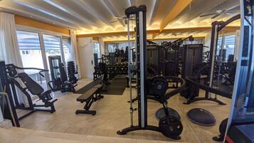 Un gimnasio con equipo de ejercicio diverso, ventanas amplias y un ventilador de techo.