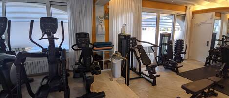 Un gimnasio con diversos equipos de ejercicio, como cintas de correr, elípticas y máquinas de pesas.