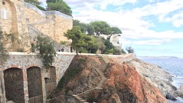 Un edificio costero de piedra con una escalera que lleva a una terraza con vistas al mar.