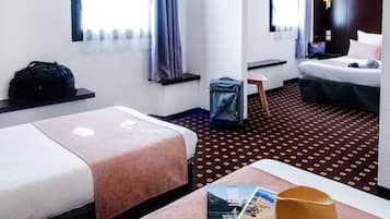 A hotel room with two beds, a desk, a chair, a suitcase, a handbag, and a magazine on the bed.