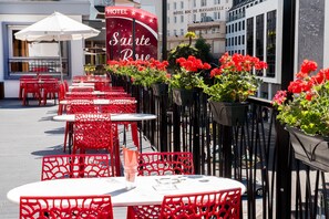 Outdoor seating with red chairs and white tables, a sign for 'Sainte Rose', and a building with 'HOTEL ROC DE MASSABIELLE' in the background. - Hotel Sainte Rose (Lourdes)