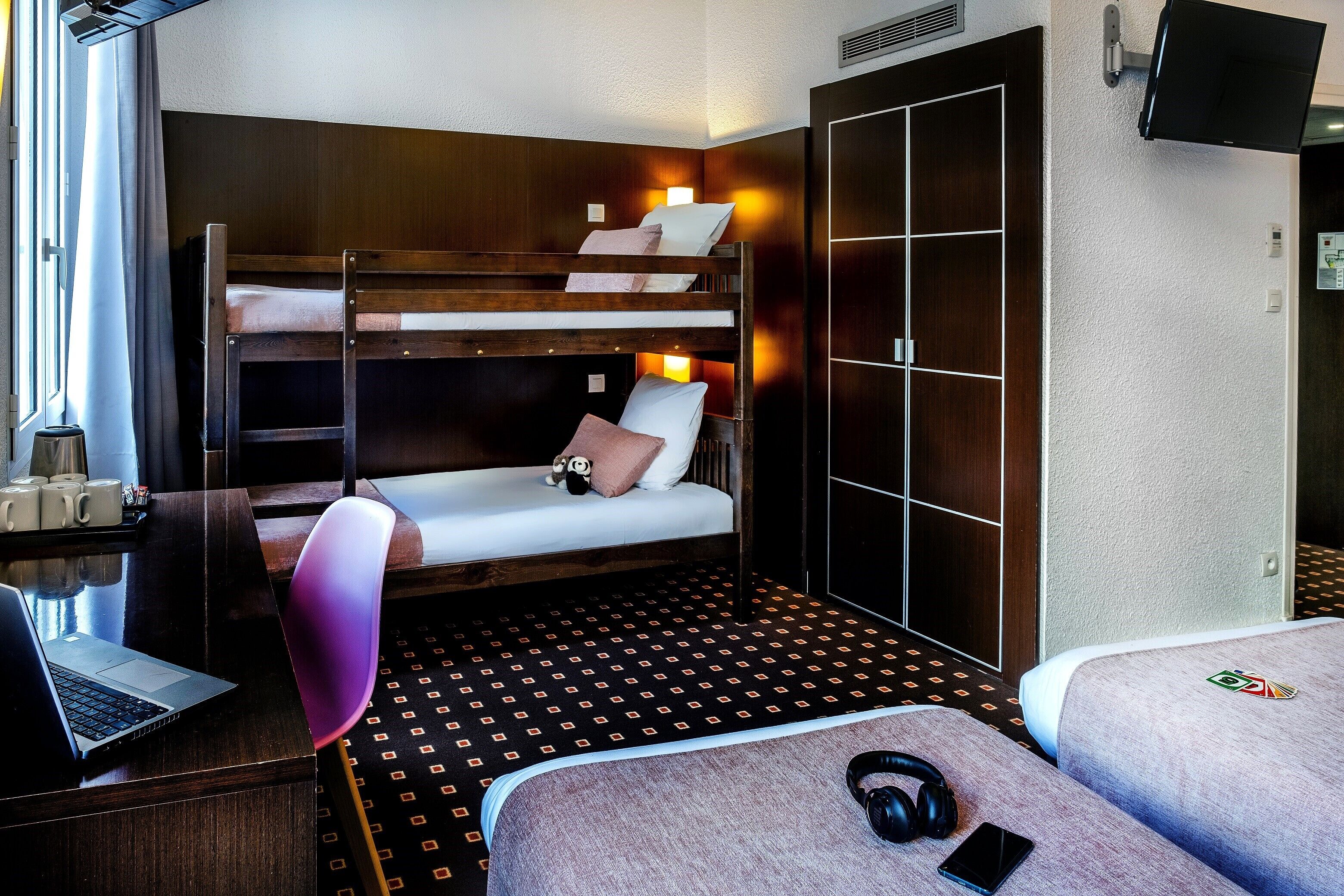 A bunk bed with a desk and chair, a laptop, and a pair of headphones on the bed.