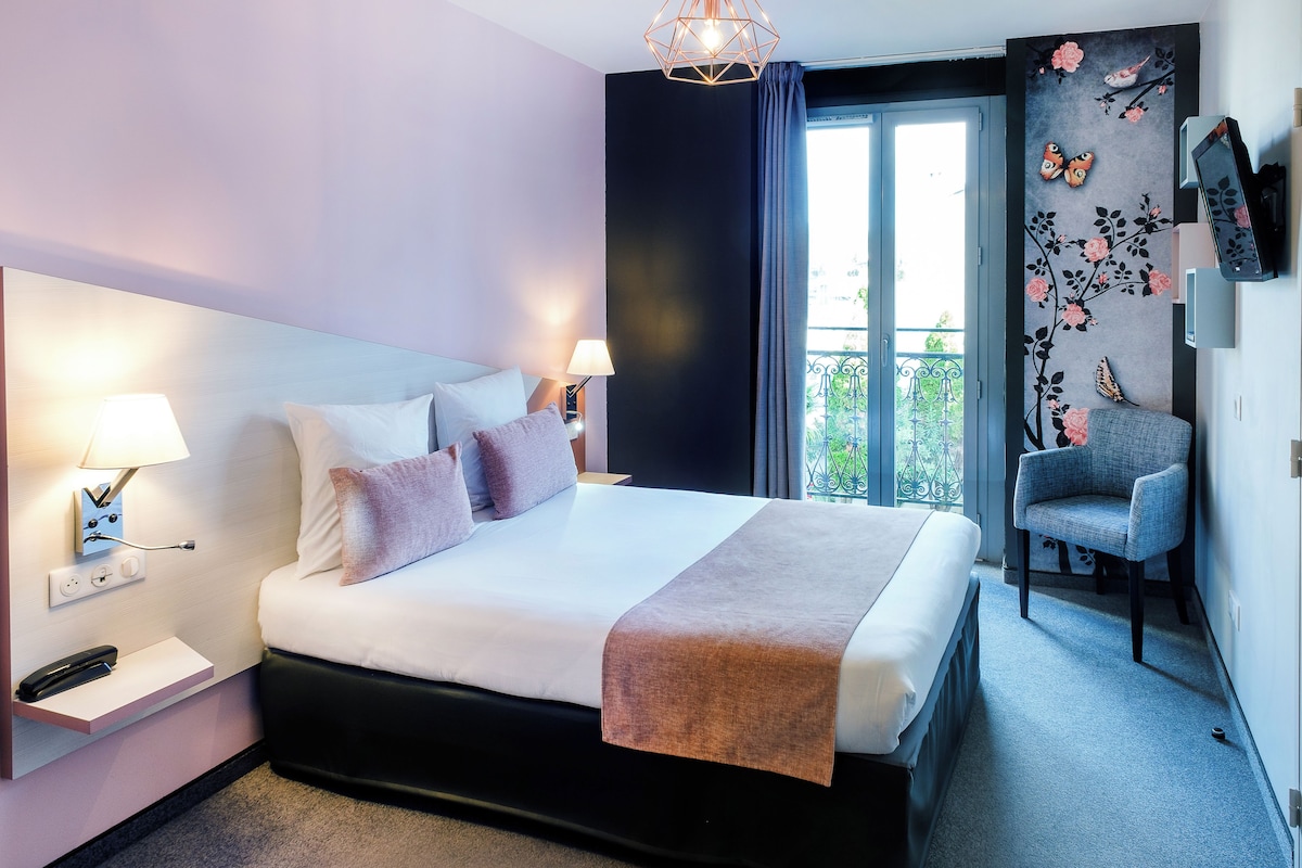 A modern hotel room with a large bed, bedside lamps, a flat-screen TV, a chair, and a balcony with a view.