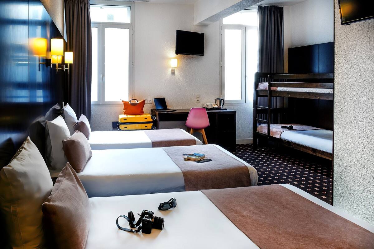 A hotel room with two beds, a desk with a laptop, a TV, and a bunk bed.